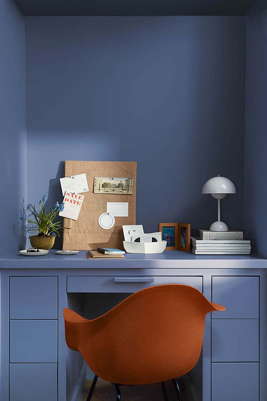 A modern red office chair sits in a home office painted in Blue Nova 825, with built-in shelving, cabinetry and in-set desk topped with a pegboard, plants, books and a modern domed white desk lamp